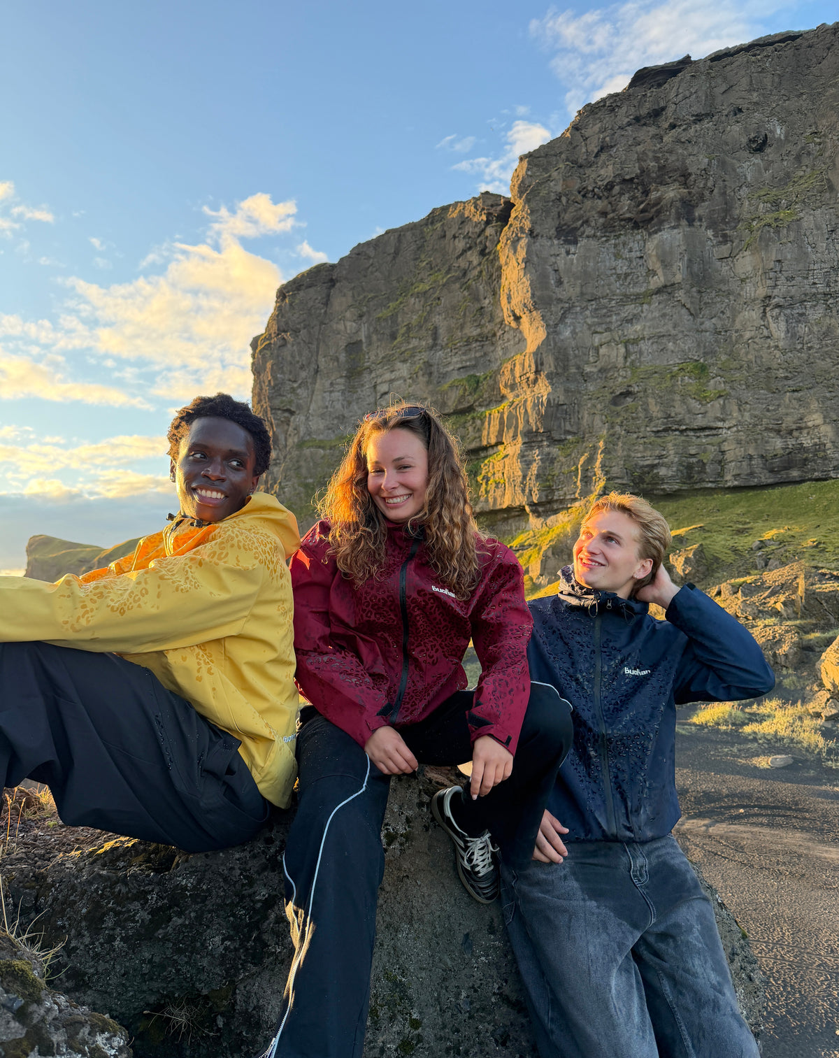 Three friends sitting on a rocky cliff, the one on the left in the water reactive cheetah rain jacket in yellow