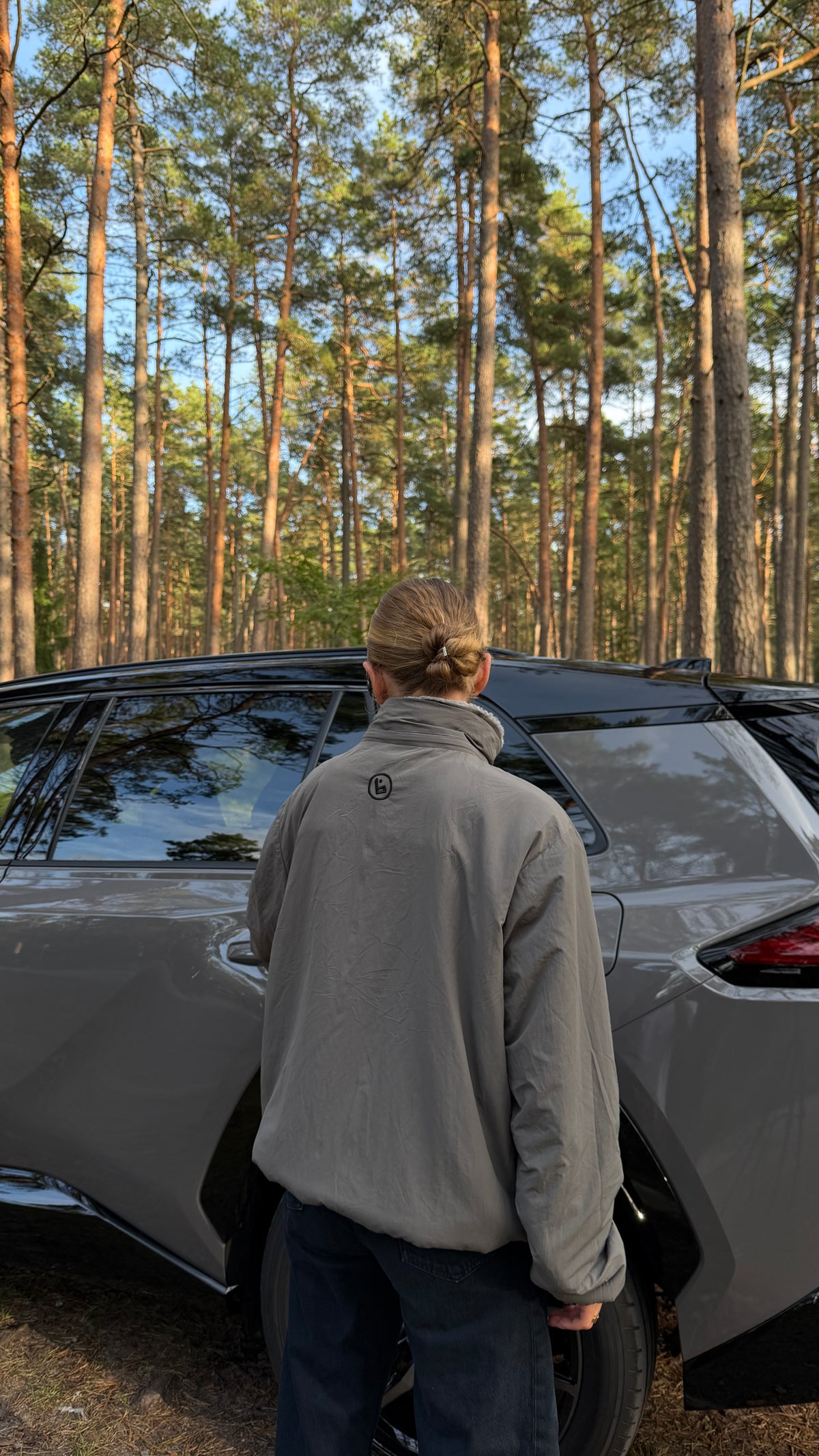 Back view of a model in the reversible Buchan fleece in grey with the collar up, pine forest behind