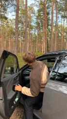 Model getting into a car wearing the reversible Buchan fleece in brown, side view in a pine forest