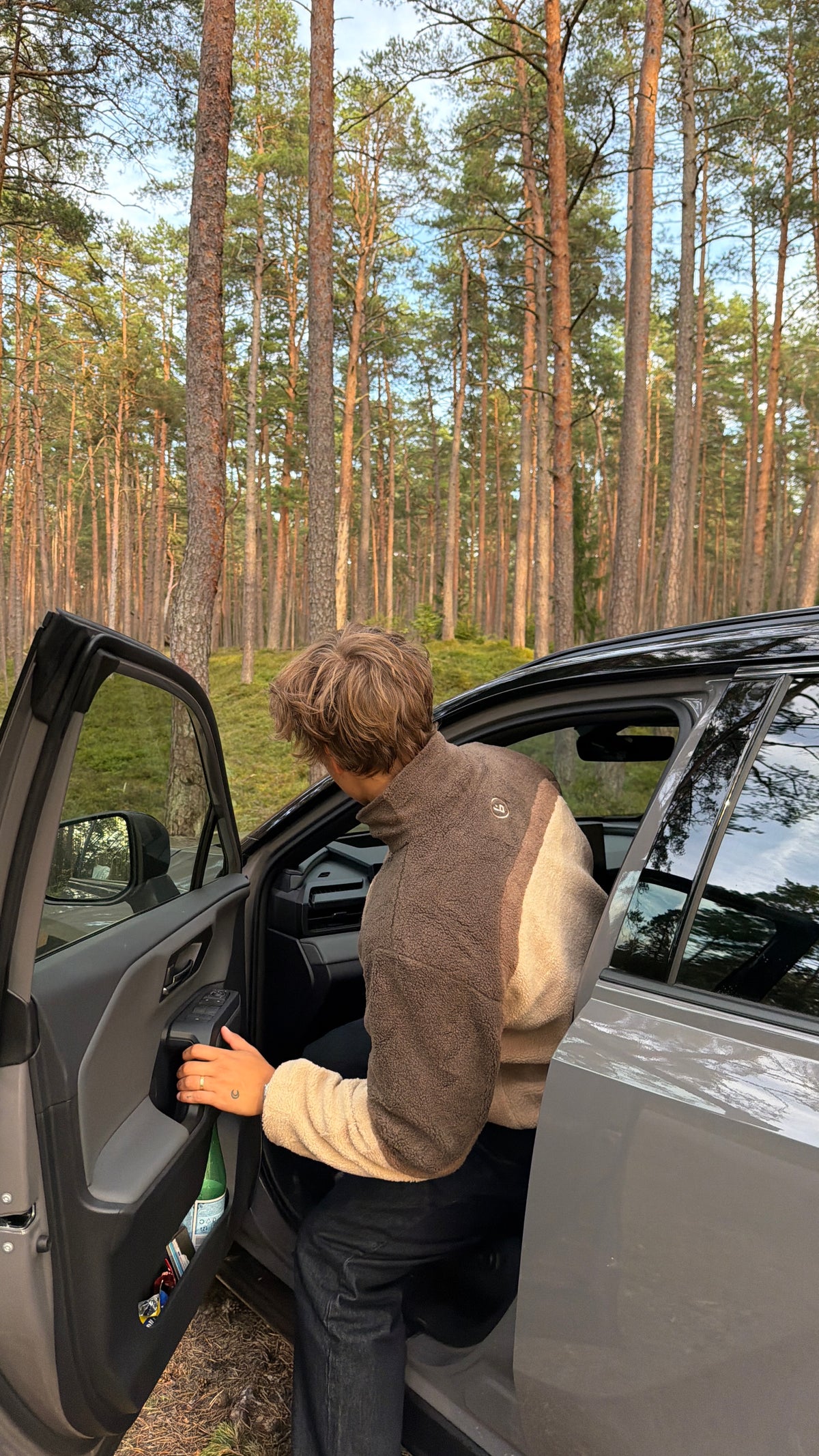 Model getting into a car wearing the reversible Buchan fleece in brown, side view in a pine forest