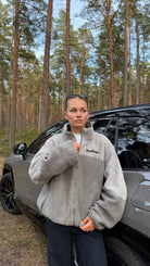 Model wearing the reversible Buchan fleece in grey, sherpa side out, standing by a car in a forest