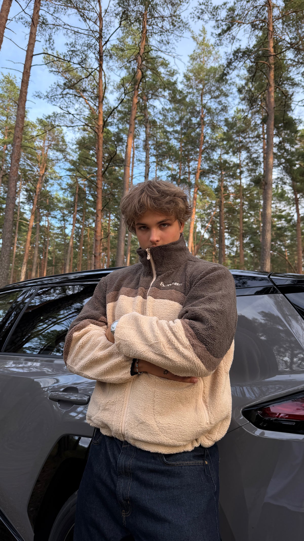 Model in the reversible Buchan fleece in brown with the collar zipped up, standing by a car in a forest