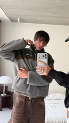 Mirror selfie of a model wearing the reversible Buchan fleece in khaki with the zip half open
