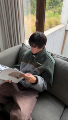 Model reading on a sofa in the reversible Buchan fleece in khaki, green and grey sherpa side out