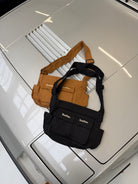 Small cargo bag in black on a car bonnet next to the brown version, top-down view