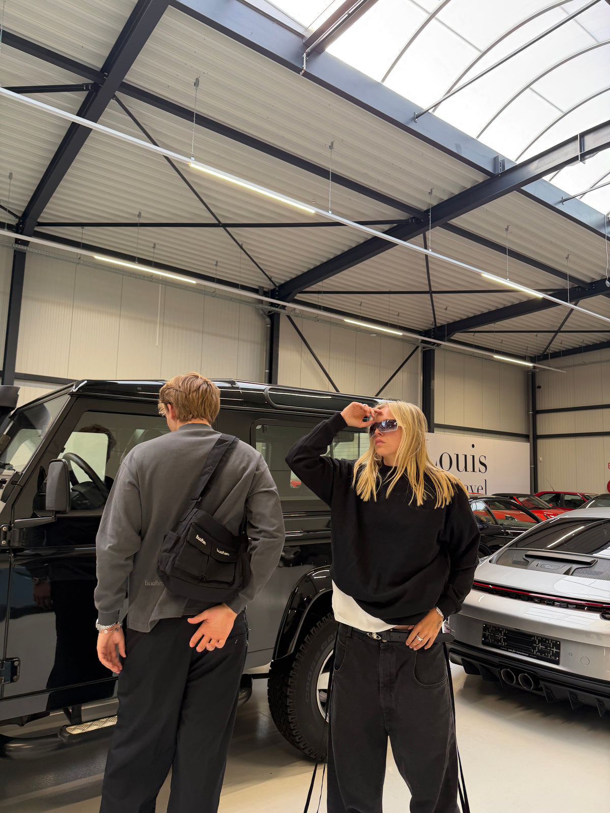 Two models in a car showroom, one carrying the Buchan small cargo bag in black across the chest