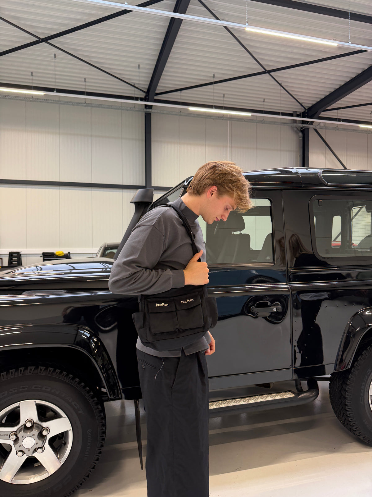 Model in a car showroom wearing the Buchan small cargo bag in black across the body