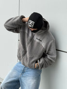 Model leaning against a wall in the reversible Buchan fleece in grey, sherpa side with the hood up