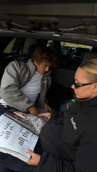 Two models sitting in a car boot reading a magazine, one wearing the reversible Buchan fleece in grey
