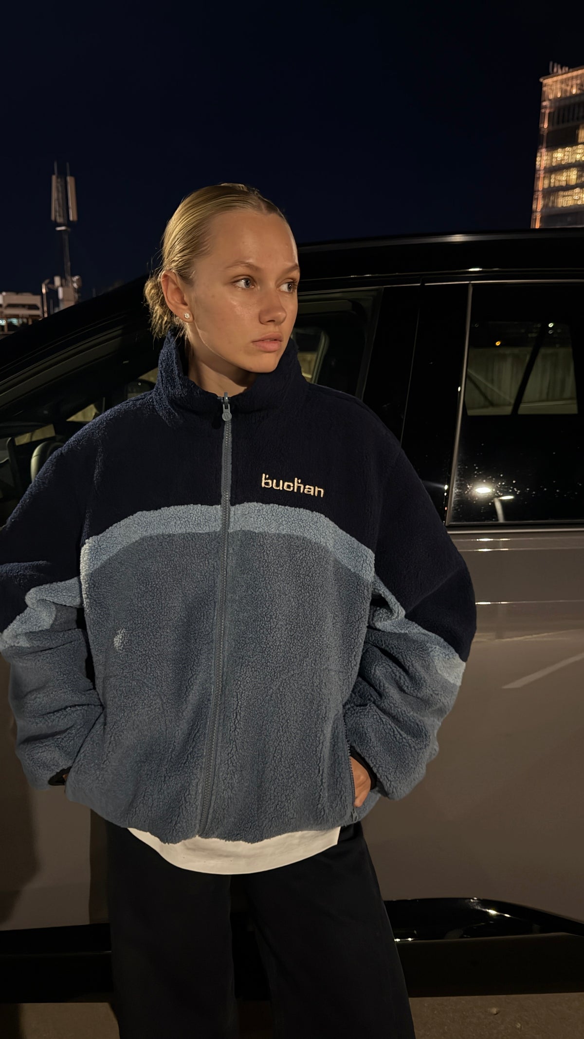 Model at night wearing the reversible Buchan fleece in blue, navy and blue sherpa zipped to the collar