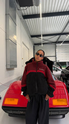 Model posing in front of a red sports car wearing the reversible Buchan fleece in red