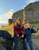 Three friends sitting on a rocky cliff, the one on the left in the water reactive cheetah rain jacket in yellow